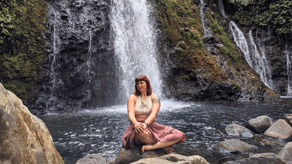 girl sitting in waterfall wearing skirt, smiling